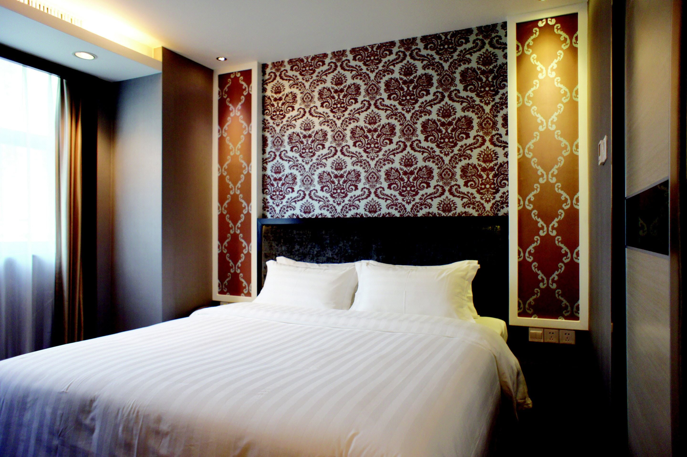 Une chambre d’hôtel avec un grand lit, un papier peint à motifs et une table de chevet avec une lampe.
