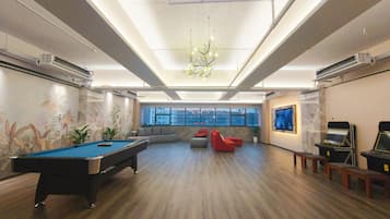 A spacious room with a pool table, comfortable seating, and large windows offering a view of the city.