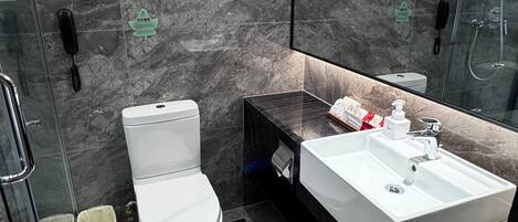 A modern bathroom with a marble wall, a glass shower enclosure, a white toilet, and a white sink with a mirror above it.