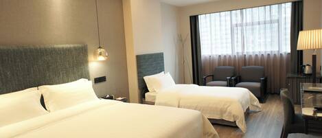 A hotel room with two beds, a desk with a lamp, a chair, and a large window with curtains.