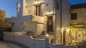 A white building with a stone facade, a chimney, and a door with a window above it. - Villa Aerino (Kissamos)