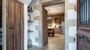 A rustic kitchen with stone walls, wooden cabinets, and a stone archway leading to a dining area. - Villa Aerino (Kissamos)