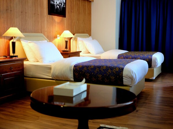 A hotel room with two beds, wooden floors, and a small round table. - Hotel Norbuling (Thimphu)