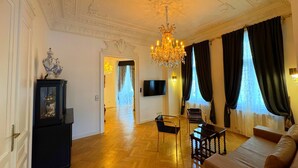 A spacious living room with a chandelier, a sofa, two chairs, a TV, and a wooden floor. - 7th Heaven Vienna Center Apartments (Vienna)