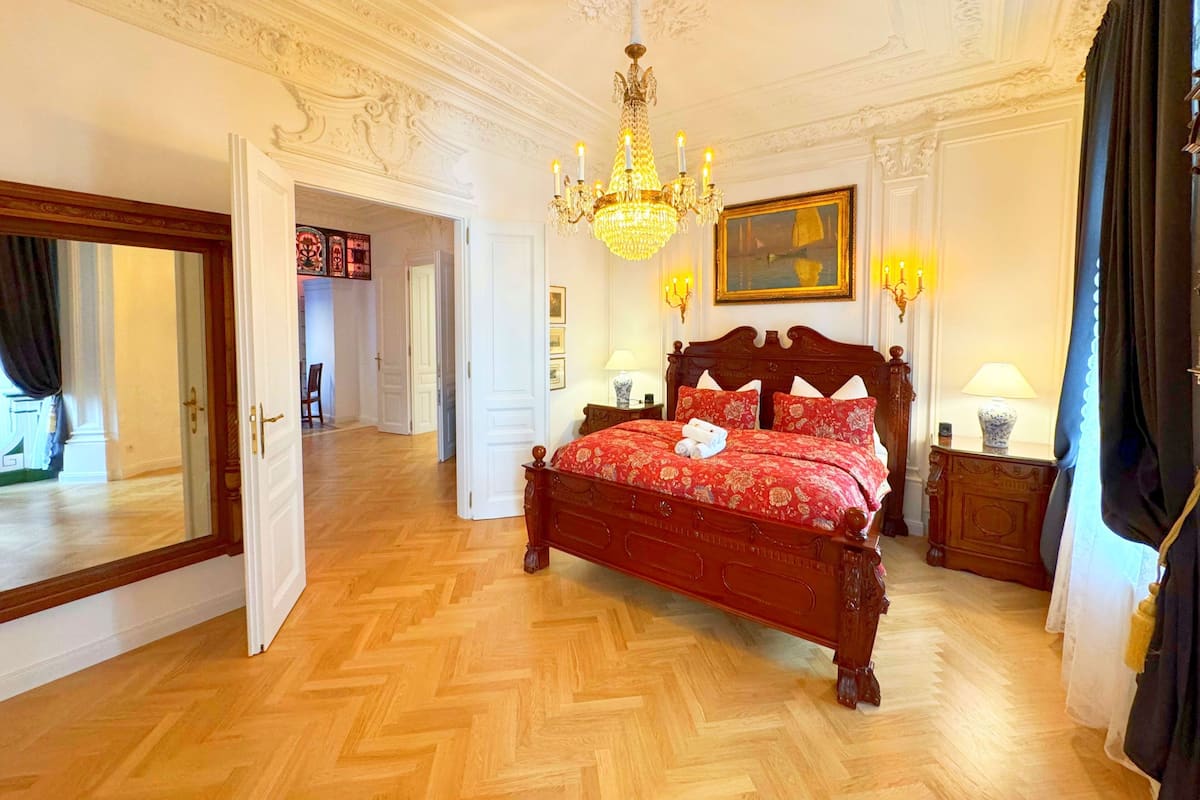 Un dormitorio espacioso con una cama grande, un techo ornamentado y una araña.