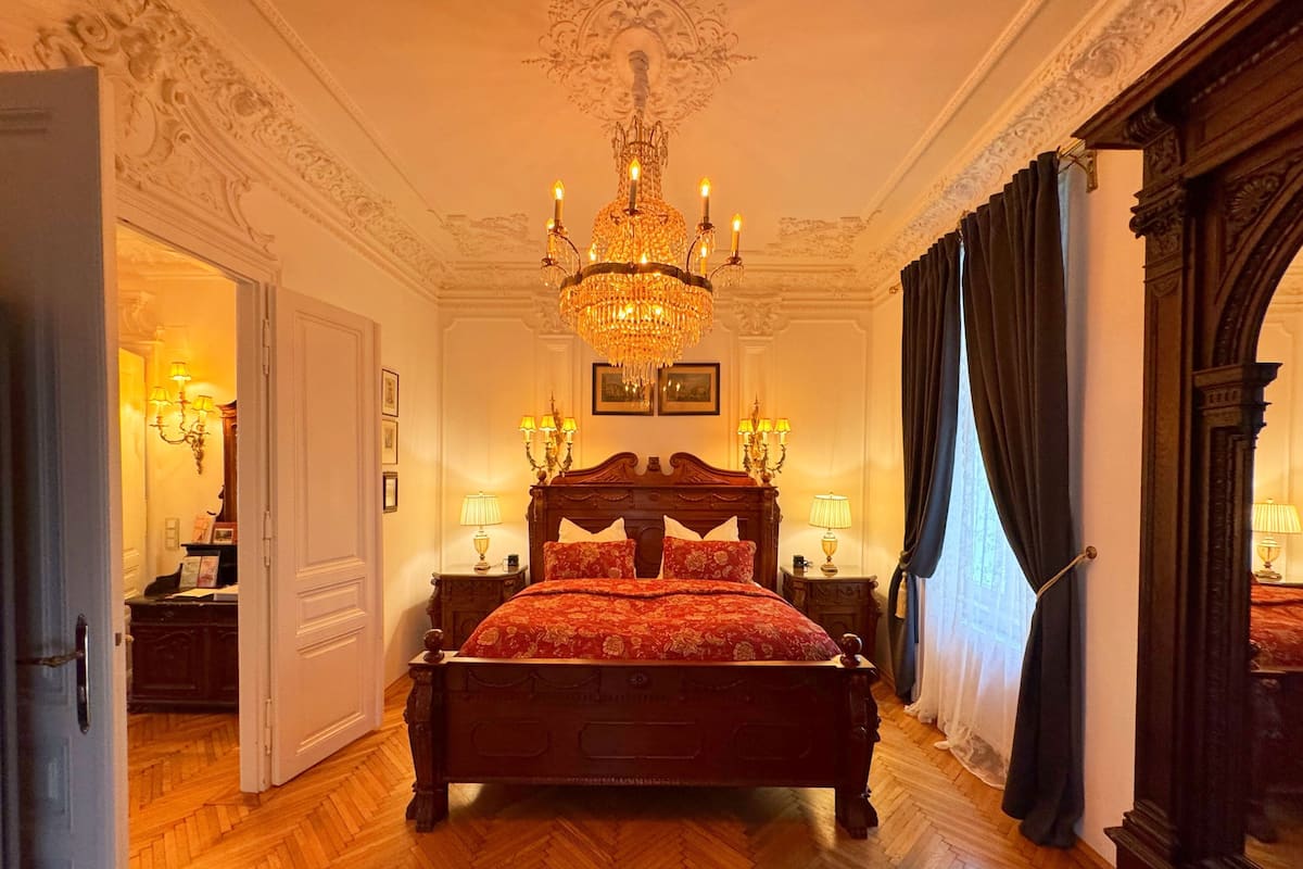 Un dormitorio amplio con una cama grande y decorada, un candelabro y un espejo.