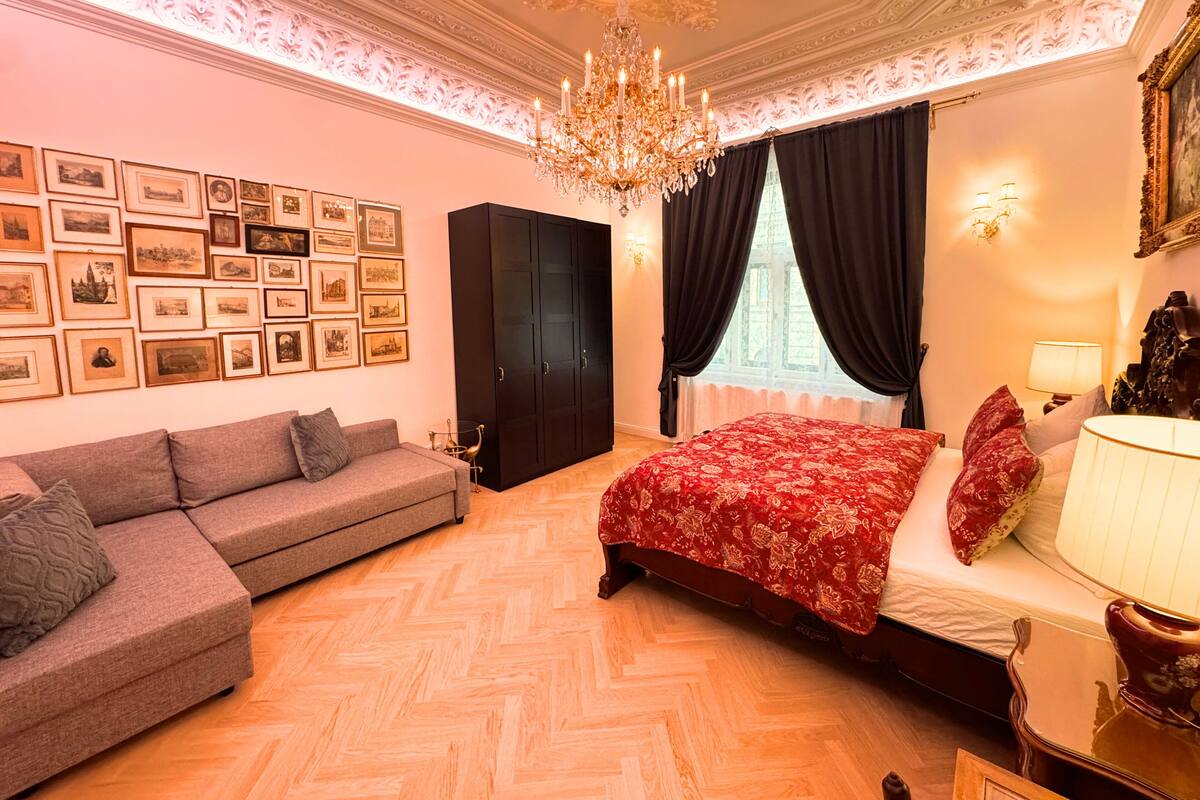 Un dormitorio con una cama grande, un sofá, un armario, una araña y cuadros enmarcados en la pared.