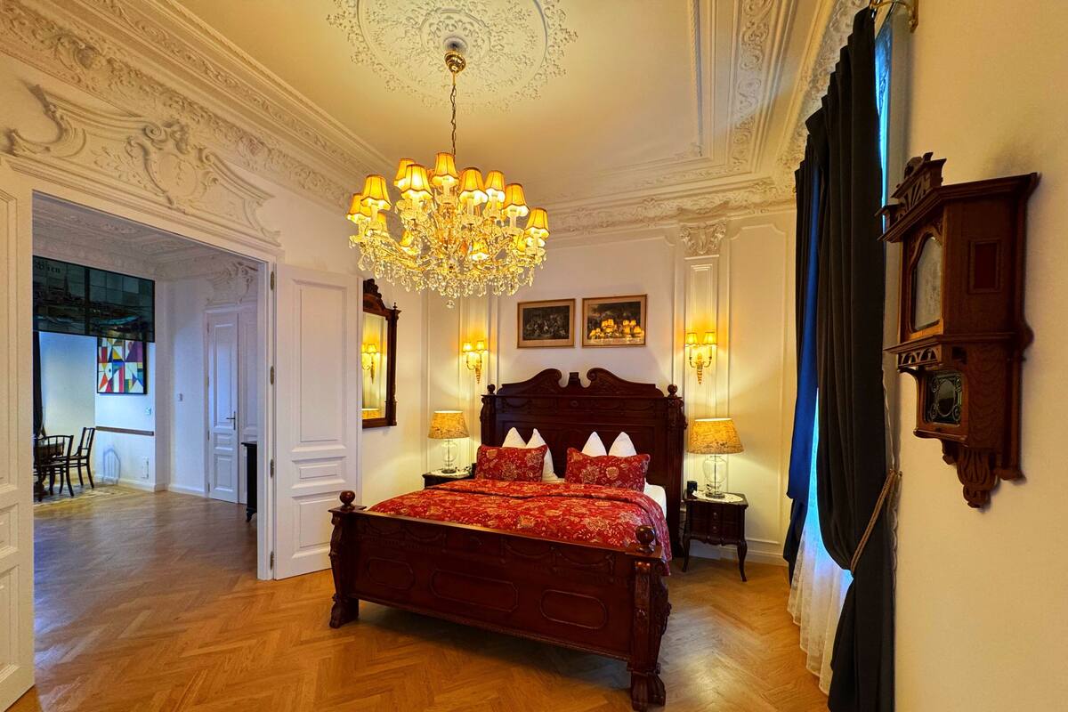 Un dormitorio espacioso con una cama grande de madera, techo ornamentado y una araña.