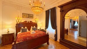 Une chambre à coucher luxueuse, dotée d’un grand lit, d’un plafond richement décoré et d’un miroir imposant.
