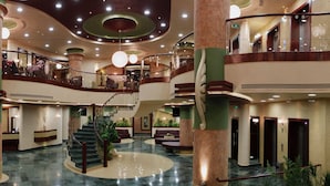 A spacious hotel lobby with multiple floors, a central staircase, and a large chandelier. - Saint Gabriel Hotel (Bethlehem)