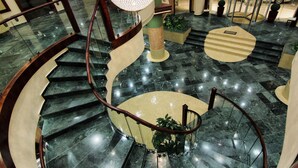 A spiral staircase with a glass railing, a roundabout, and a central column with a spherical light fixture. - Saint Gabriel Hotel (Bethlehem)