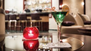 A bar area with a glass table, a red spherical object, and a green cocktail with an orange garnish. - Saint Gabriel Hotel (Bethlehem)