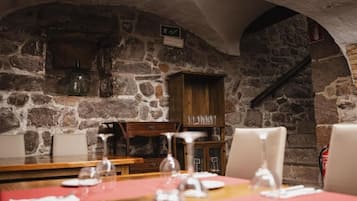 Interior de parets de pedra amb taules preparades per sopar, un armari de fusta i una escala.