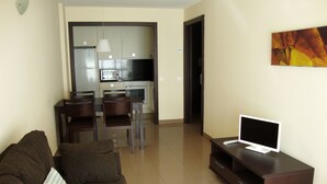 A living room with a brown sofa, a flat-screen TV on a wooden stand, and a dining area with chairs and a kitchen in the background. - Apartamentos Canillo Pie de Pistas 3000 (Canillo)