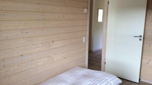 A room with wooden walls, a bed with white bedding, and a door leading to another room. - Blokhus Golfcenter (Pandrup)
