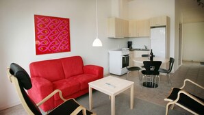 A modern living room with a red sofa, a white coffee table, and black chairs. There is a kitchen area with a white refrigerator, stove, and cabinets. - Blokhus Golfcenter (Pandrup)