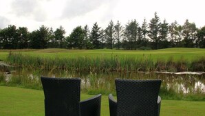 Two wicker chairs facing a pond with a golf course and trees in the background. - Blokhus Golfcenter (Pandrup)