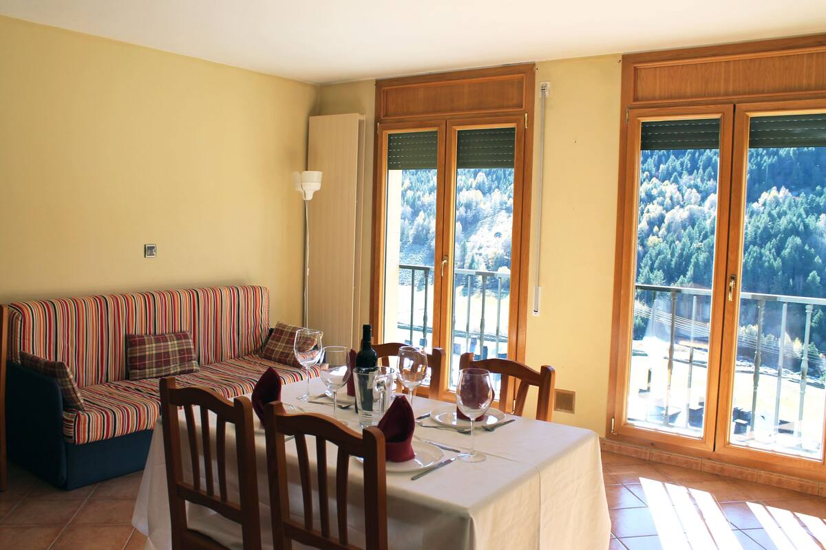 A dining area with a table set for four, a sofa, and large windows with a view of trees.