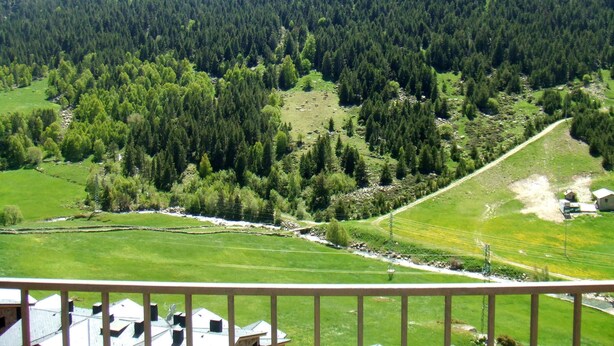 A mountainous landscape with dense forests, a river, and a few buildings in the foreground. - Aptos Colells (Bordes d'Envalira)