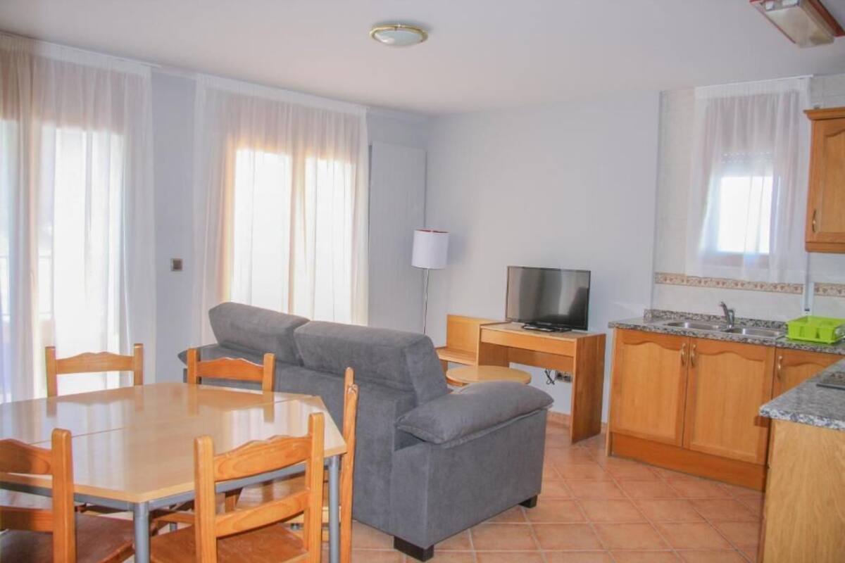 A compact living space with a dining table, sofa, TV, and kitchenette.