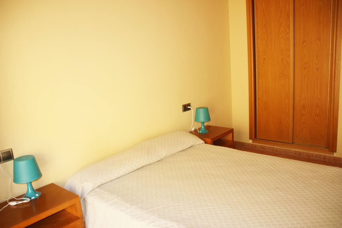 A bedroom with a bed, two nightstands, a wooden wardrobe, and a wall socket.