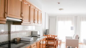 A modern kitchen with wooden cabinets, a granite countertop, and a dining area with a table and chairs. - Aptos Colells (Bordes d'Envalira)