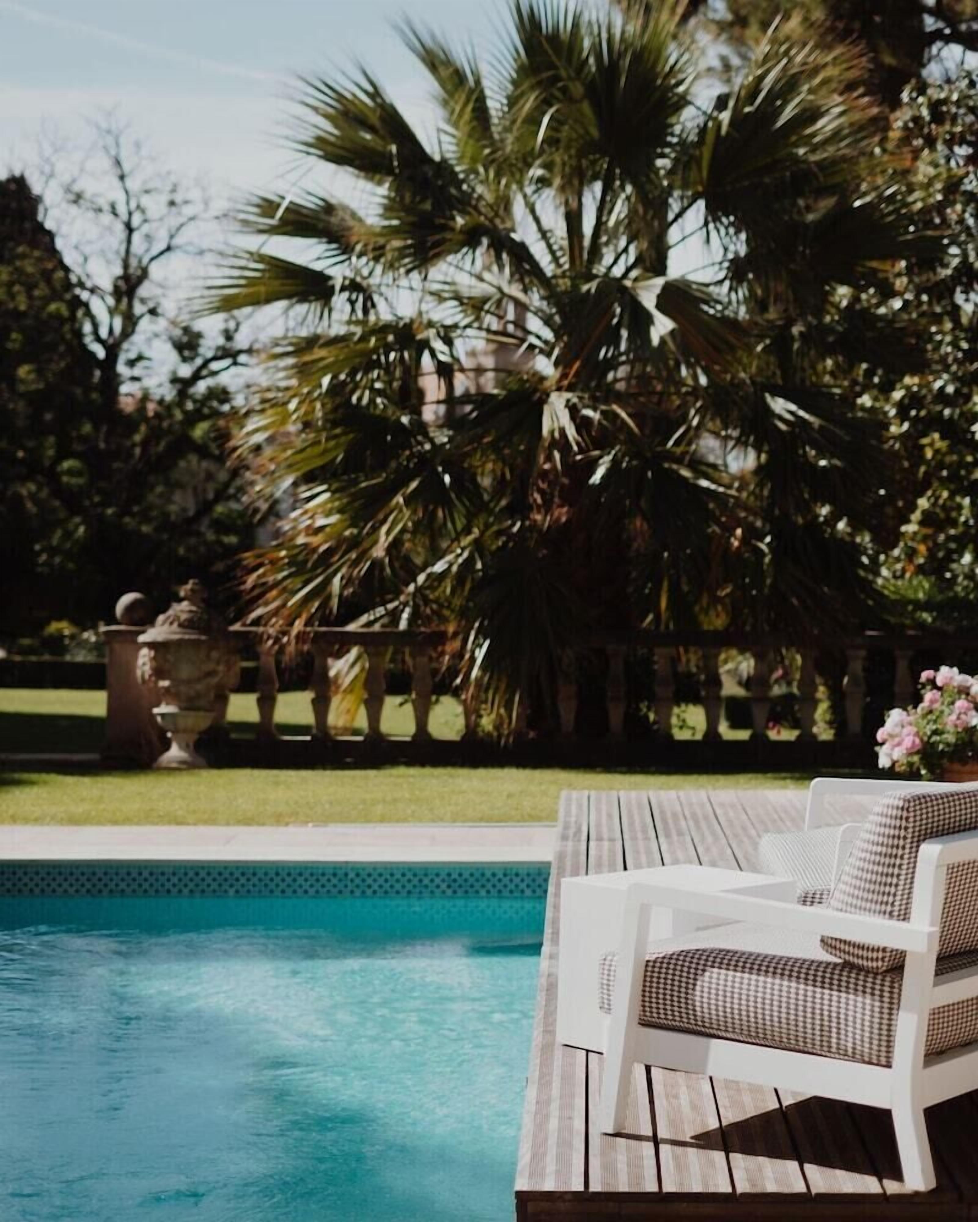 A poolside area with a wooden deck, a white lounge chair, and a palm tree.