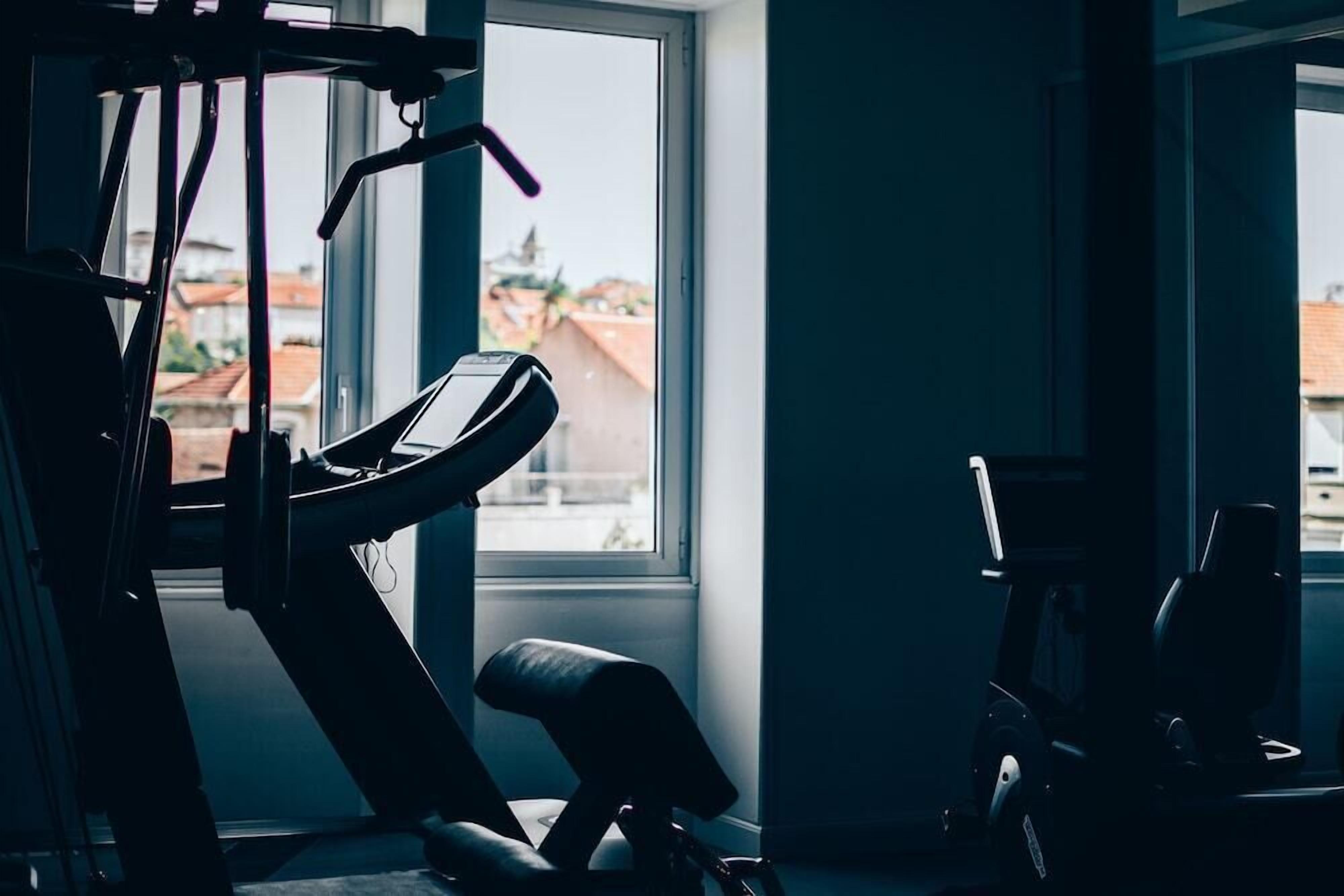 A gym with exercise equipment, a bench, and large windows offering a view of buildings outside.