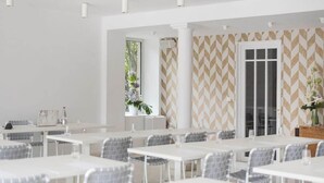 A modern dining area with white tables and chairs, a patterned wall, and a large window with plants. - La Villa Guy (Béziers)
