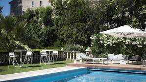 A pool area with a clear blue pool, white lounge chairs, and a pergola with white umbrellas. - La Villa Guy (Béziers)
