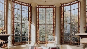 Una habitación con techo curvo, amplias ventanas de vitral, un conjunto de sofás y un otoman redondo.