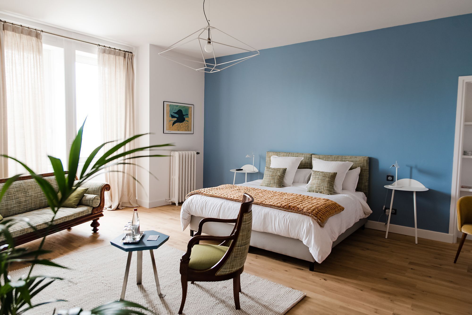 Une chambre à coucher avec un lit, une chaise, une petite table, un radiateur et une plante.
