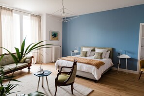 A bedroom with a bed, a chair, a small table, a radiator, and a plant. - La Villa Guy (Béziers)