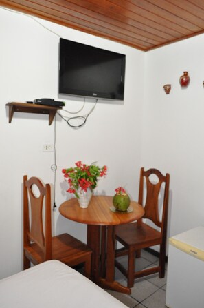 En liten matplats med ett träbord, två stolar, en tv som är monterad på väggen och en liten hylla ovanför bordet.