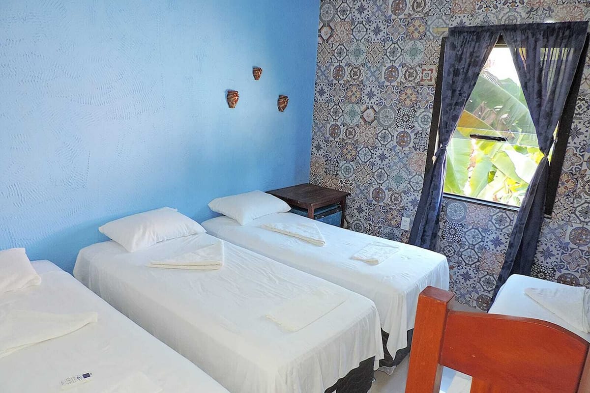 A room with three single beds, a small wooden table, and a window with patterned curtains.