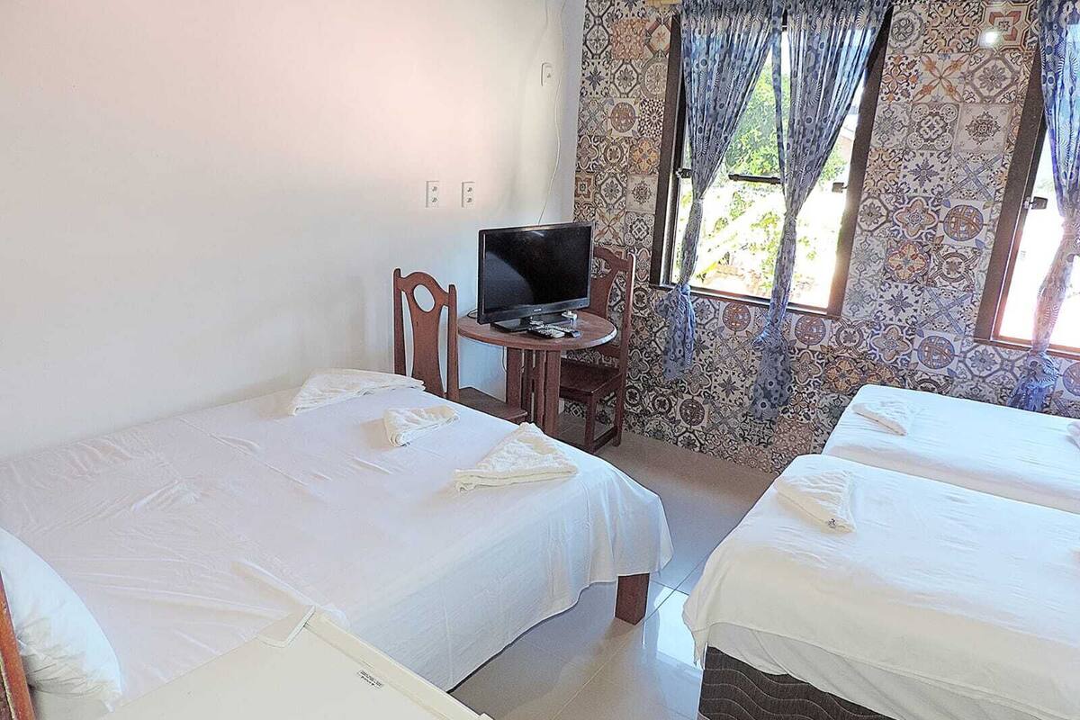 A hotel room with two beds, a TV, a small table, and a window with patterned curtains.