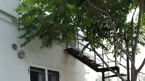 A patio area with a table and chairs, a tree, and a white building with a sliding glass door. - Le Sorbole (Matera)