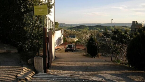 A paved driveway leading to a parked car, surrounded by greenery and a view of distant hills. - Le Sorbole (Matera)