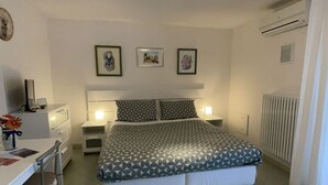 A bedroom with a bed, bedside tables, a desk, and chairs. There are framed pictures on the wall and an air conditioning unit. - Le Sorbole (Matera)