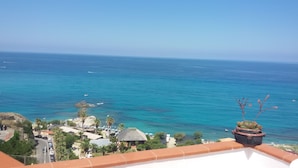 Blick auf die Küste mit blauem Meer, einem Strand mit Sonnenschirmen und einem Blumentopf auf dem Balkon.
