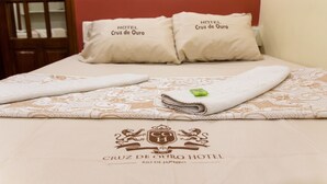 Una cama bien hecha con una colcha estampada y almohadas con la etiqueta "HOTEL Cruz de Ouro".