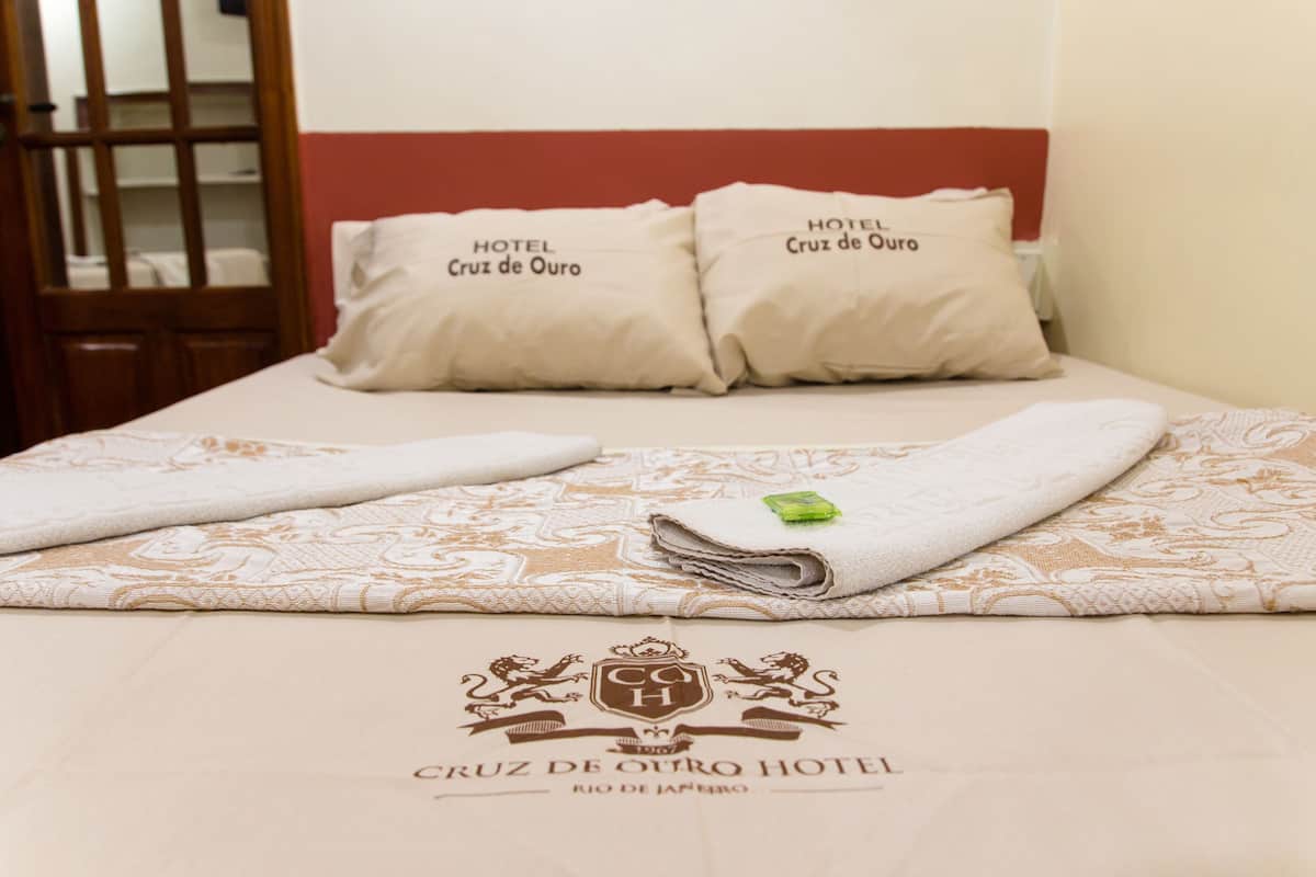 A neatly made bed with a patterned bedspread and pillows labeled "HOTEL Cruz de Ouro."