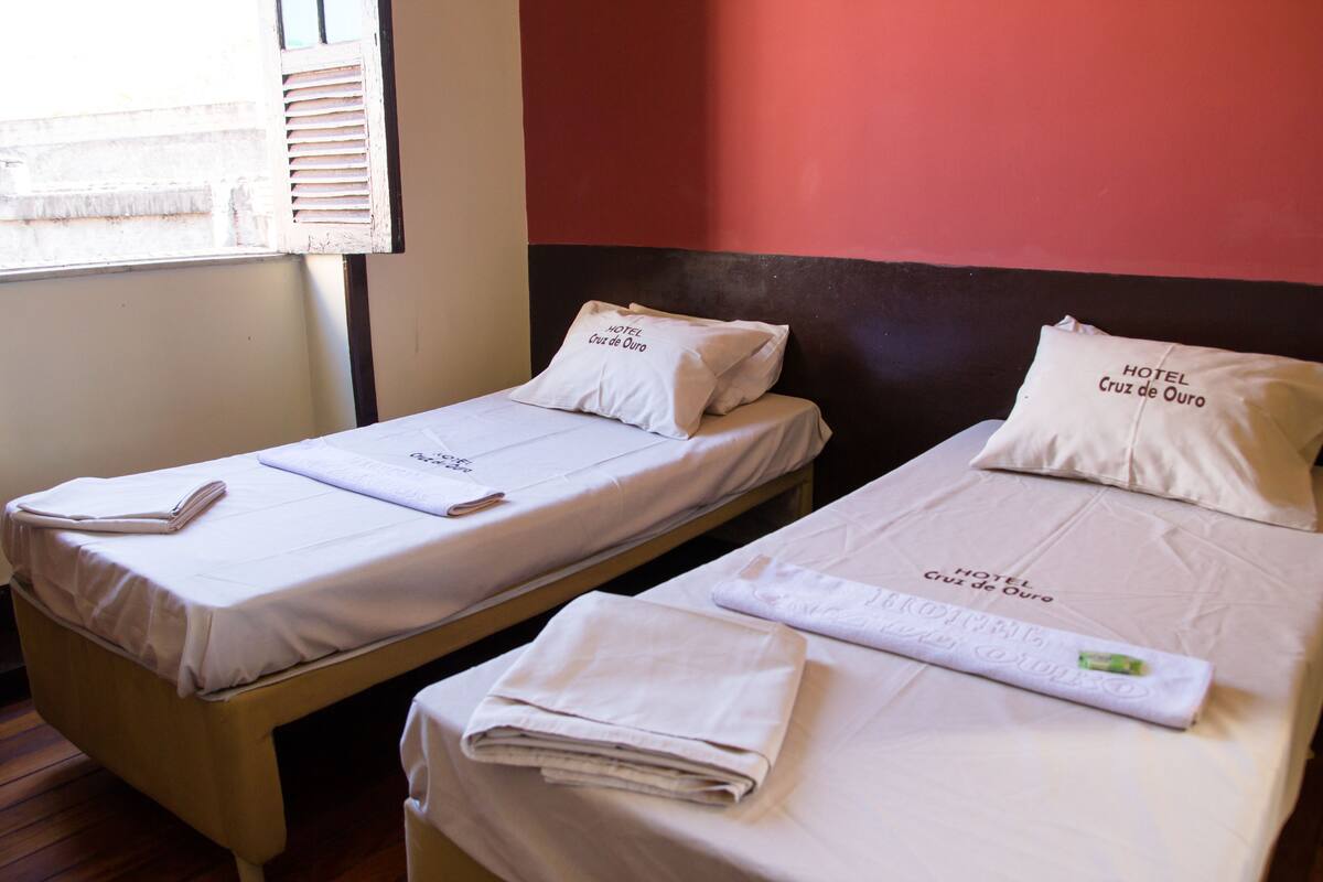 Two single beds with white bedding and pillows labeled "HOTEL Cruz de Ouro".