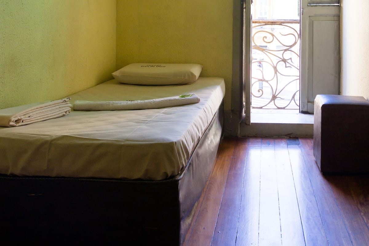 A small room with a bed, a chair, and a door leading to an outdoor area.