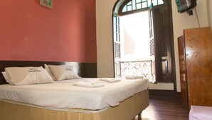 Una habitación de hotel con una cama, un armario de madera, un televisor y una ventana con contraventanas abiertas.