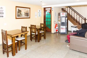 A lobby with a wooden table and chairs, a framed picture on the wall, a green door labeled 'Salão de Café', and a water dispenser. - Hotel Cruz de Ouro (Rio de Janeiro)