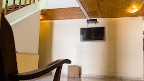 Una habitación con una escalera de madera, un televisor de pantalla plana en la pared y un taburete pequeño de madera.