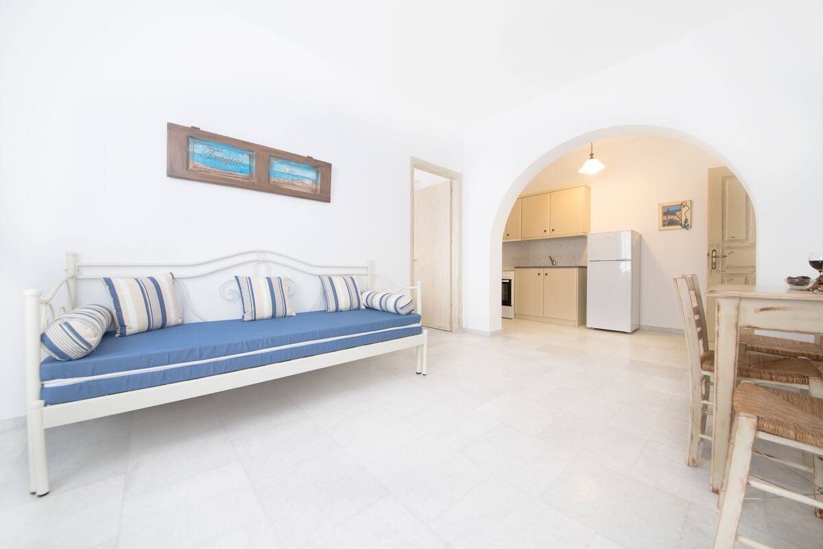 A white sofa with blue cushions in a bright room with white walls and a tiled floor.