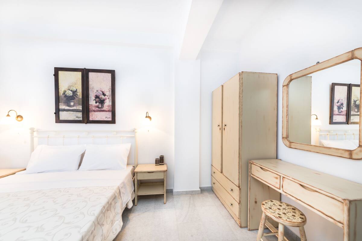 A bedroom with a bed, bedside table, dresser, and a large mirror.