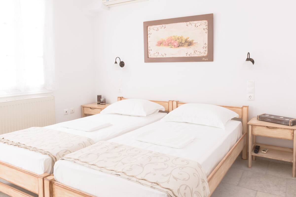A double bed with a wooden headboard, two bedside tables, a wall-mounted light fixture, and a framed floral artwork.